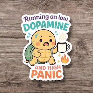Könnte beinhalten: Ein Aufkleber mit einer Comic-Schildkröte, die besorgt aussieht und eine Kaffeetasse hält. Der Text lautet "Running on low DOPAMINE AND HIGH PANIC" in Lila, Türkis und Orange. Die Schildkröte ist gelb mit einem grünen Panzer.