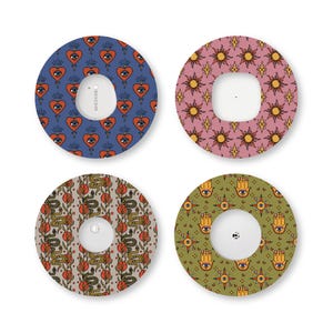 May include: Four circular adhesive patches for medical devices, each featuring a distinct pattern: blue with red hearts and eyes, pink with yellow suns, beige with green snakes and red flowers, and olive green with yellow hamsa hands and eyes.