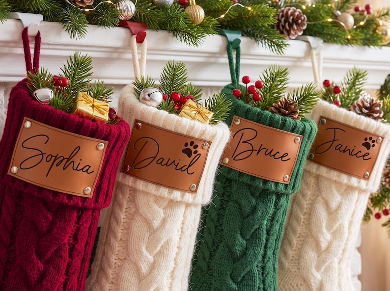 May include: Four cable-knit Christmas stockings in burgundy, cream, and forest green, each featuring a personalized tan leather patch with names Sophia, David, Bruce, and Janice, accented with pine sprigs, red berries, and small gift boxes.