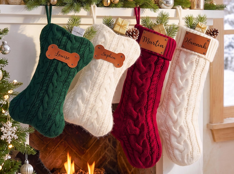 May include: Four cable-knit Christmas stockings in dark green, cream, burgundy, and white. The green and cream stockings feature bone-shaped leather tags with the names Louise and Sophia. The burgundy and white stockings have rectangular leather tags with the names Martin and Hannah.