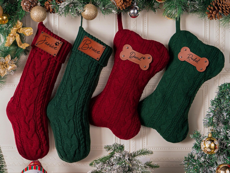 May include: Four cable-knit Christmas stockings in deep red and forest green. Two stockings are traditional boot-shaped with rectangular leather tags labeled Janice and Bruce. Two are bone-shaped with leather tags labeled David and Rachel.