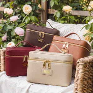 May include: Four rectangular vanity cases in dark brown, tan, burgundy, and beige, each featuring a top handle, gold-tone double zippers, and a central rectangular patch with gold-embossed initials reading ST, DF, CH, and BR respectively.