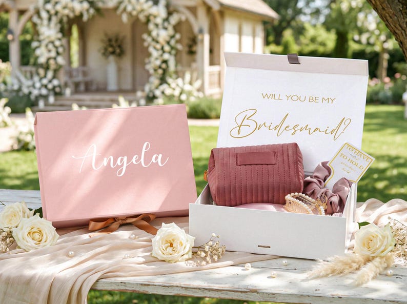 May include: A pink gift box with the name "Angela" in white script, next to an open box with a cosmetic bag, scrunchies, and a card that says "To Have and to Hold". The open box has the text "Will You Be My Bridesmaid?"