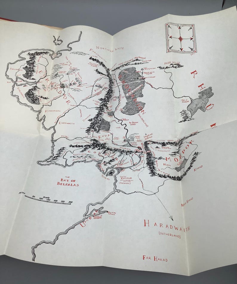 Puede incluir: Un mapa detallado de una tierra ficticia, con intrincadas ilustraciones de monta&ntilde;as, r&iacute;os y asentamientos. El mapa es principalmente en blanco y negro, con acentos rojos para nombres de lugares y caracter&iacute;sticas clave.