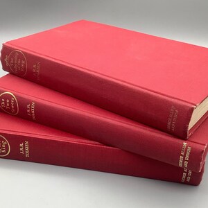 Puede incluir: Una pila de tres libros de tapa dura rojos. Los t&iacute;tulos son "La Comunidad del Anillo", "Las Dos Torres" y "El Retorno del Rey". Todos los libros son de J.R.R. Tolkien, con t&iacute;tulos dorados en los lomos.