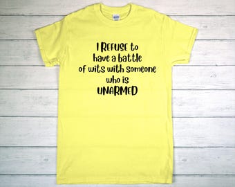 May include: A yellow t-shirt with the text "I REFUSE to have a battle of wits with someone who is UNARMED" in black lettering. The shirt is made of a soft material and has short sleeves.