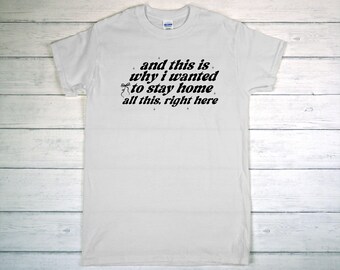 May include: A white t-shirt with the text "and this is why I wanted to stay home all this, right here" in black script. The shirt is made of a soft material and has short sleeves.