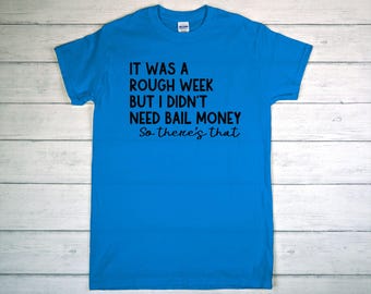 May include: A bright blue t-shirt with the text "IT WAS A ROUGH WEEK BUT I DIDN'T NEED BAIL MONEY So there's that" in black. The shirt is made of a soft material and has a crew neck.