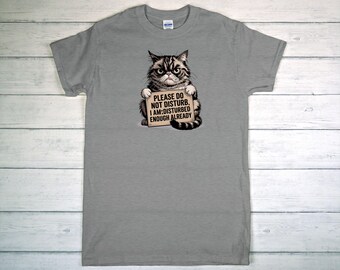 May include: A gray t-shirt featuring a grumpy cat illustration holding a sign. The sign reads "PLEASE DO NOT DISTURB, I AM DISTURBED ENOUGH ALREADY". The cat is black and brown with an angry expression.