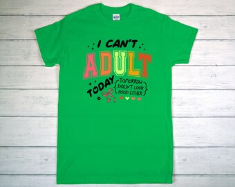 May include: A bright green t-shirt with the text "I can't adult today" in a colorful design. The word "adult" is in pink, orange, and green. The phrase "Tomorrow doesn't look good either" is also included.