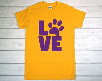 May include: Mustard yellow t-shirt with a purple paw print and the word "LOVE" in purple block letters. The shirt is made of a soft material and has a crew neck.