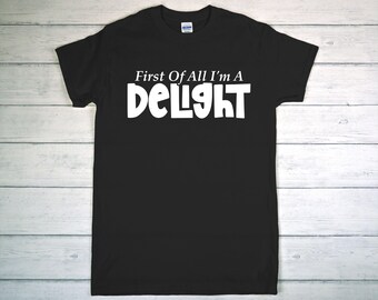 May include: Black t-shirt with the white text "First Of All I'm A Delight" in a bold, playful font. The shirt is made of a soft material and has a crew neck. A casual, everyday wear tee.