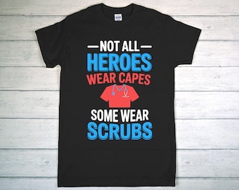 May include: Black t-shirt with the text "NOT ALL HEROES WEAR CAPES SOME WEAR SCRUBS" in white, blue, and red. A red scrub top graphic with a stethoscope is centered on the shirt. The shirt is made of a soft material.