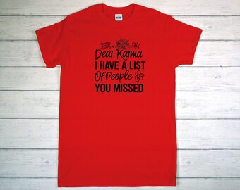 May include: A bright red t-shirt with the text "Dear Karma I Have A List Of People You Missed" in black. The text is accompanied by floral and decorative elements. The shirt is made of a soft material.
