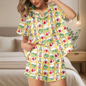 May include: Yellow pajama set featuring a repeating pattern of green Yoshi characters and red and white egg designs. The short-sleeved top and shorts have white trim. The pajamas are made of a soft, comfortable material.