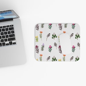May include: A white mouse pad with a repeating pattern of colorful flowers. The flowers are a variety of pinks, reds, oranges, yellows, and purples. The mouse pad is on a white surface.