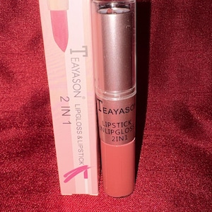 May include: A 2-in-1 lipstick and lip gloss product by Teayason. The product is in a rectangular box and a cylindrical tube. The box and tube are primarily pink and brown. The text "2 IN 1 LIPGLOSS & LIPSTICK" is printed on the box.