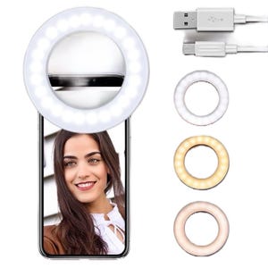 May include: A white LED ring light attached to a smartphone, illuminating a woman's face. The image shows the ring light with three different color temperature settings and a USB charging cable. The ring light is designed for selfies and video recording.