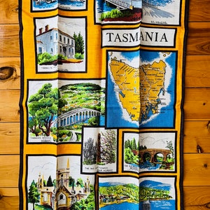 Puede incluir: Una toalla de t&eacute; amarilla con un mapa de Tasmania, Australia. La toalla presenta im&aacute;genes de varios puntos de referencia, incluidos puentes, iglesias y edificios. El texto "TASMANIA" y "AUSTRALIA" est&aacute; impreso en la toalla.