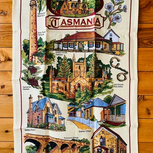 Puede incluir: Un pa&ntilde;o de cocina de estilo vintage con ilustraciones de monumentos hist&oacute;ricos de Tasmania, Australia. El pa&ntilde;o es de color crema con acentos rojos, marrones y verdes. El texto "Historic Tasmania" est&aacute; impreso en una pancarta roja en la parte superior del pa&ntilde;o.