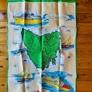 Puede incluir: Un pa&ntilde;o de cocina vintage con un mapa de Tasmania, Australia. El mapa es verde con l&iacute;neas blancas y puntos blancos. El pa&ntilde;o tambi&eacute;n presenta un barco amarillo y rojo, una br&uacute;jula y el texto "TASMANIA" en letras amarillas. El pa&ntilde;o est&aacute; hecho de lino puro y hecho en China.