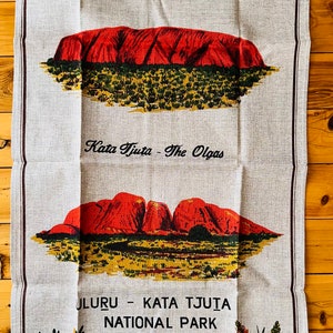 Op de afbeelding: Een theedoek met een beige achtergrond met illustraties van Uluru en Kata Tjuta, ook bekend als Ayers Rock en The Olgas, in Centraal-Australi&euml;. De tekst "Uluru - Kata Tjuta National Park, Central Australia" is op de theedoek gedrukt.