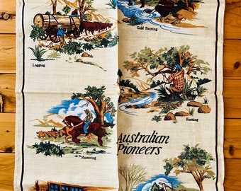 Op de afbeelding: Een vintage theedoek met een beige achtergrond en kleurrijke illustraties van Australische pioniers. De tekst "Greetings from NAROOMA" staat bovenaan de theedoek. De illustraties tonen scènes van houtkap, goud zoeken, jagen, verzamelen, scheren en mijnbouw.