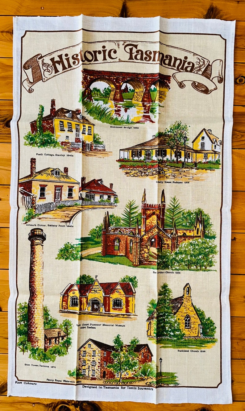Puede incluir: Un pa&ntilde;o de cocina vintage con fondo beige e ilustraciones coloridas de edificios hist&oacute;ricos en Tasmania. El texto "Historic Tasmania" est&aacute; impreso en letras marrones en la parte superior de la toalla. La toalla presenta ilustraciones de edificios como el puente de Richmond, Port Cottage, Emily House, Arthur Circus, East Tower, Penny Royal y Backland Church.