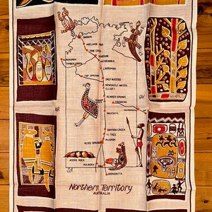 Op de afbeelding: Een vintage theedoek van linnen met een kaart van het Northern Territory van Australi&euml; met verschillende steden en dorpen aangegeven. De kaart is omgeven door gestileerde Aboriginal kunstontwerpen in rood, bruin en geel.