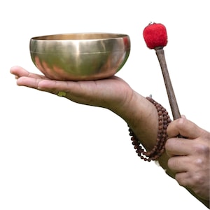Op de afbeelding: Een bronzen zangkom wordt in één hand gehouden, met een houten hamer met een rode vilten kop in de andere. Een streng bruine kralen is om de pols gewikkeld. De kom is rond en heeft een glad oppervlak.