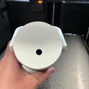K&ouml;nnte beinhalten: Ein wei&szlig;es, kreisf&ouml;rmiges Objekt mit einem kleinen, dunklen Loch in der Mitte. Das Objekt wird in einer Hand gehalten und scheint ein Bestandteil eines gr&ouml;&szlig;eren Ger&auml;ts zu sein. Das Objekt hat eine strukturierte Oberfl&auml;che und ist wahrscheinlich aus Kunststoff.