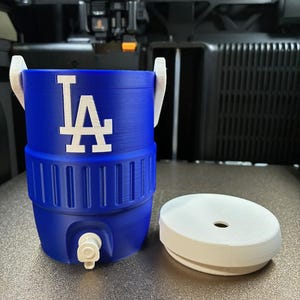 K&ouml;nnte beinhalten: Ein blau-wei&szlig;er Wasserk&uuml;hler mit dem Logo der Los Angeles Dodgers. Der K&uuml;hler hat einen Wasserhahn und einen wei&szlig;en Deckel. Der K&uuml;hler ist etwa 30 cm hoch und hat einen Durchmesser von 20 cm.