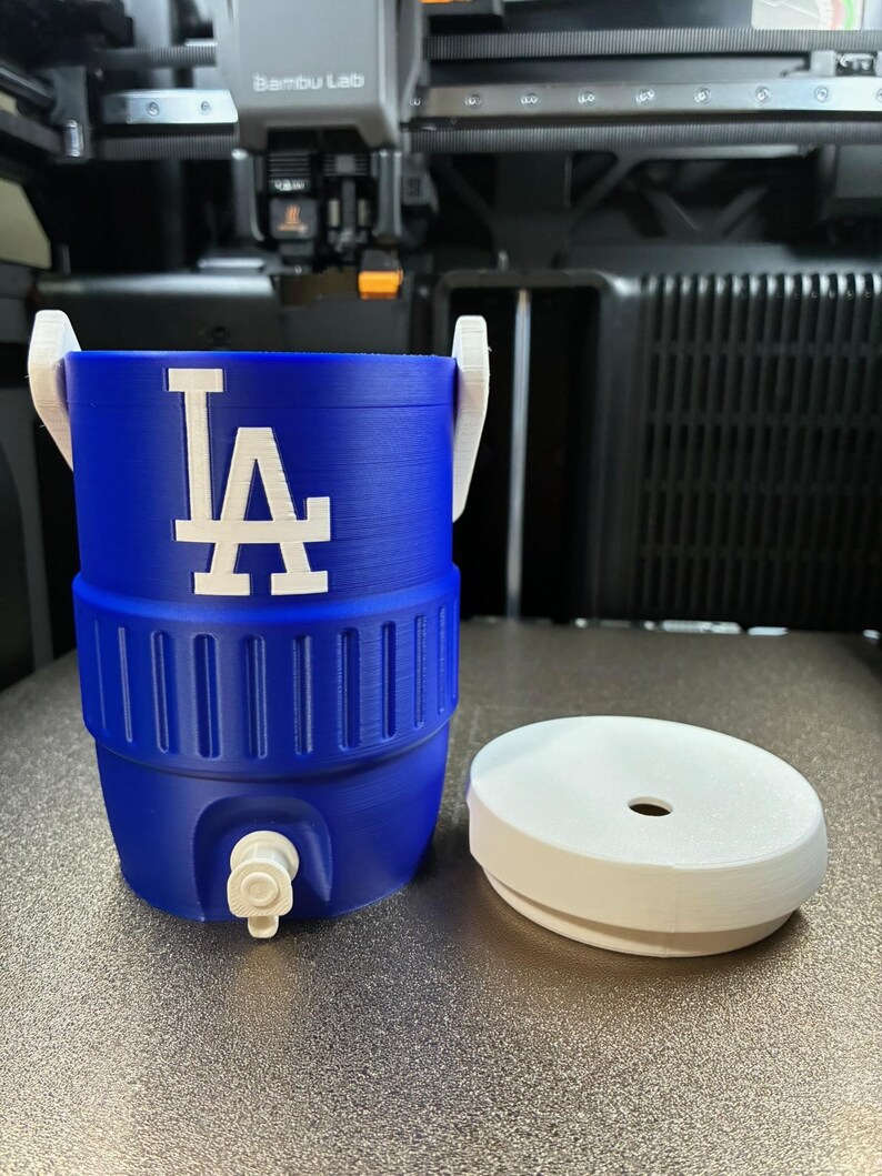 K&ouml;nnte beinhalten: Ein blau-wei&szlig;er Wasserk&uuml;hler mit dem Logo der Los Angeles Dodgers. Der K&uuml;hler hat einen Wasserhahn und einen wei&szlig;en Deckel. Der K&uuml;hler ist etwa 30 cm hoch und hat einen Durchmesser von 20 cm.