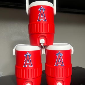 K&ouml;nnte beinhalten: Drei rote Wasserk&uuml;hler mit wei&szlig;en Deckeln und Griffen sind gestapelt. Jeder K&uuml;hler zeigt das Logo der Los Angeles Angels in Blau und Wei&szlig;. Die K&uuml;hler haben einen Wasserhahn zum Ausgeben von Fl&uuml;ssigkeiten.
