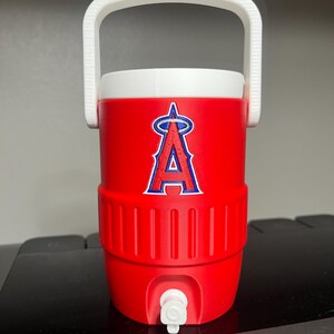 K&ouml;nnte beinhalten: Ein roter Wasserk&uuml;hler mit wei&szlig;em Griff und Deckel. Der K&uuml;hler zeigt das Logo der Los Angeles Angels in Blau und Wei&szlig;. Er hat einen wei&szlig;en Wasserhahn an der Unterseite zum Ausgeben von Fl&uuml;ssigkeiten. Der K&uuml;hler ist so konzipiert, dass Getr&auml;nke kalt gehalten werden.