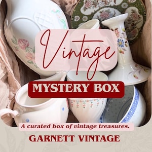 May include: A collection of ceramic items including a white pitcher with floral patterns, a decorative plate, a candlestick, and small bowls. The image features the text Vintage MYSTERY BOX, A curated box of vintage treasures, and GARNETT VINTAGE.