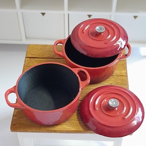 以下が含まれることがあります： ドールハウスやクラフトプロジェクトに最適な、蓋付きのミニチュア赤い鋳鉄鍋。鍋の内側は黒色で、蓋には銀色のつまみが付いています。セットには、蓋付きの鍋2つと蓋なしの鍋1つが含まれています。