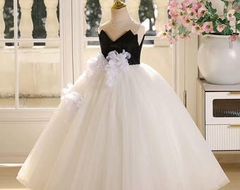 May include: A formal black and white dress for a young girl. The bodice is black with a sweetheart neckline, and the skirt is a full, flowing white tulle. White floral accents adorn the waist and shoulder.
