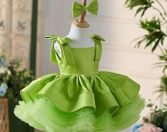 May include: A lime green dress with a matching bow headband. The dress features a square neckline, bow accents on the shoulders, and a layered skirt with a tulle underlay. The dress is displayed on a mannequin.