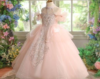May include: A pale pink formal dress with a halter neckline and a full skirt. The bodice is decorated with silver sequins and beads. The dress features a layered tulle skirt and ruffled sleeves. The dress is displayed on a mannequin.