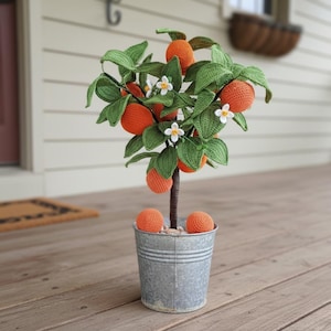 May include: A handmade crochet orange tree in a galvanised metal pot. The tree has green leaves, white flowers, and several orange crochet oranges. The tree is a decorative item, ideal for home decor.