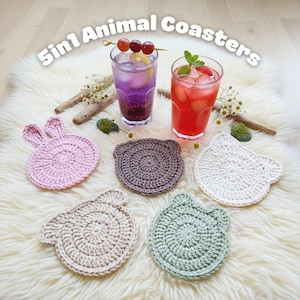 May include: Five crochet animal coasters in pink, brown, and white, with a bunny, bear, and cat design. The coasters are arranged on a fluffy white surface, with two glasses of drinks in the background. The text "5in1 Animal Coasters" is at the top.