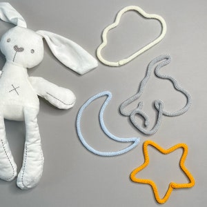 May include: A white plush bunny toy with embroidered details, surrounded by crocheted shapes: a cloud, a crescent moon, a star, and a whimsical elephant.
