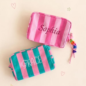 Può includere: Due astucci rettangolari con cerniera in tessuto di velluto a coste. Uno presenta strisce verticali rosa con il nome Sophia ricamato in rosa scuro. L'altro ha strisce verde acqua e rosa con il nome GRACE ricamato in filo bianco.