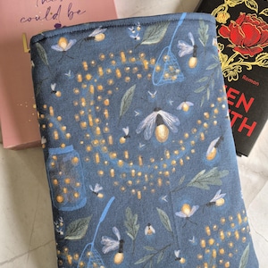 Könnte beinhalten: Eine marineblaue Bucheinbandhülle mit einem Glühwürmchenmuster. Der Stoff zeigt gelb leuchtende Glühwürmchen, ein Glas und ein Netz, mit grünen Blättern. Zum Schutz von Büchern.