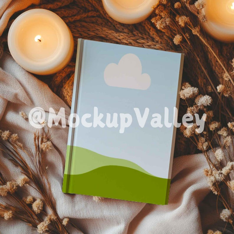 May include: A blue and green book with a white cloud and a green hill design. The book is lying on a beige blanket with dried flowers and candles.