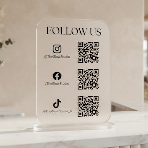 May include: A rectangular, semi-transparent acrylic sign with rounded corners, featuring the text FOLLOW US, three social media icons, corresponding handles @TheGlowStudio, /TheGlowStudio, @TheGlowStudio_S, and three distinct black QR codes.