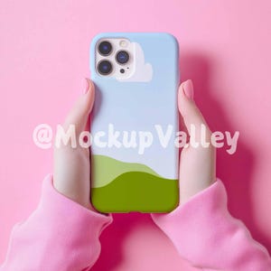 May include: A light blue phone case with a white cloud and green hills design. The case is being held by a person with pink sleeves.