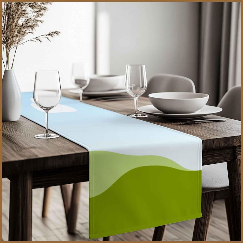 May include: A light blue and green table runner with a wavy design. The runner is on a wooden table with two wine glasses and a bowl.
