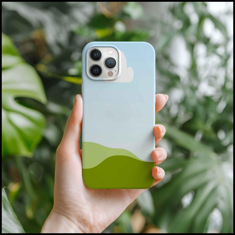 May include: A smartphone case with a landscape design. The case features a gradient sky of light blue to white, a white cloud, and green rolling hills. The case is held in a hand against a blurred green background.